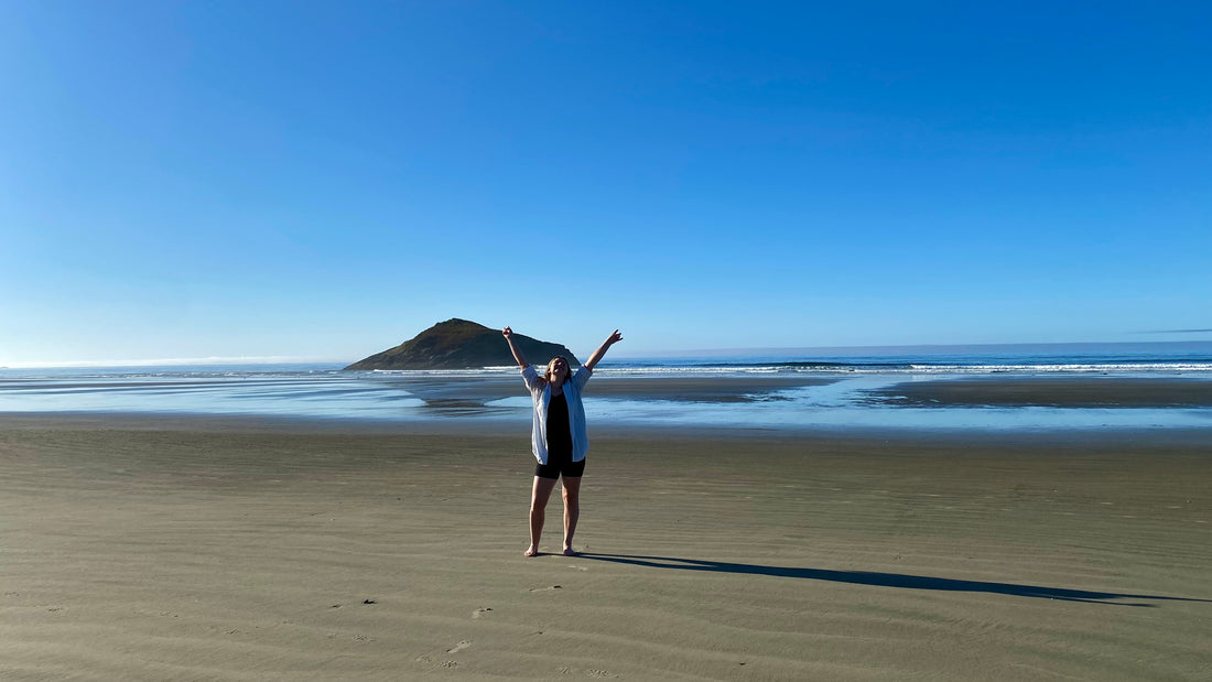 Woman standing alone on a beach looking out towards the water.